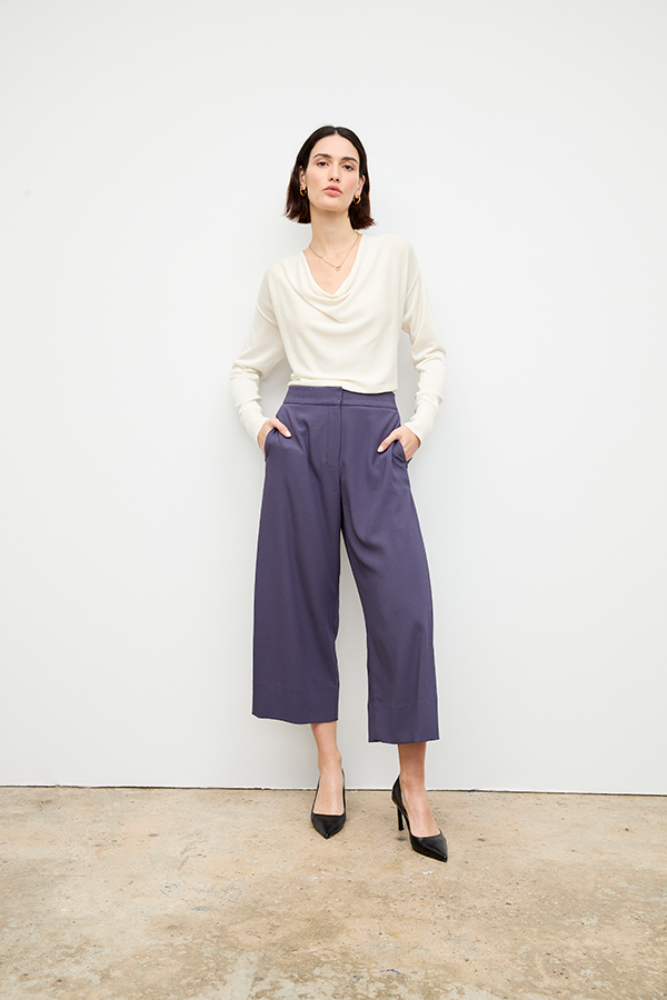 Complex on-figure image of a model in cropped purple pants and cream top, before retouch.