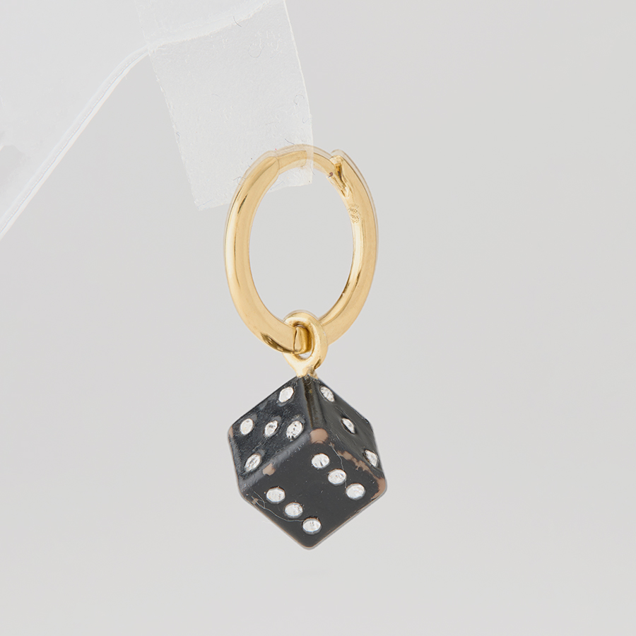 Jewelry product image of a gold hoop earring with a black dice charm, pre-retouch, showing props and product defects