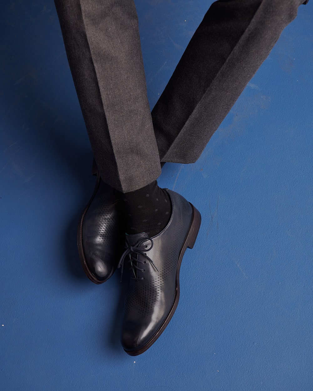 Close-up e-commerce shot of leather dress shoes on a blue backdrop, highlighting footwear details.